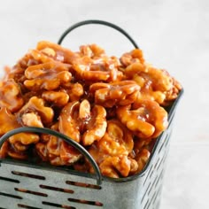 a metal basket filled with caramel cashews on top of a white table