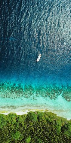 an aerial view of a boat in the water near some green trees and blue water