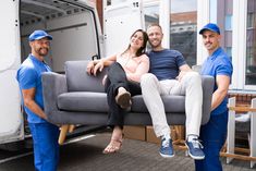 three people sitting on a couch in front of a moving truck