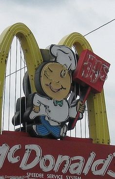 a sign for mcdonald's with a cartoon character holding a spatula in front of it