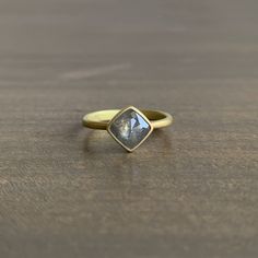 a gold ring with a labradorese stone in the center on a wooden table top