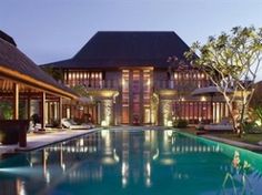 an outdoor swimming pool with lounge chairs and umbrellas next to the house at night