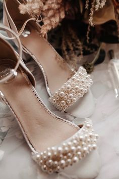 a pair of white shoes with pearls on the toes and heels are sitting next to some flowers