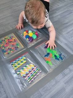 a baby crawling on the floor in front of four plastic trays filled with different colored candies