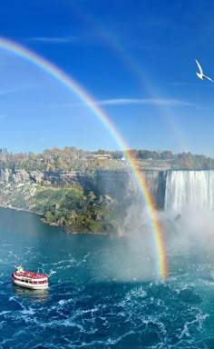 a boat in the water near a waterfall with a rainbow