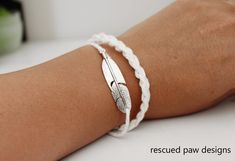 a woman's arm wearing a white bracelet with a silver feather charm on it