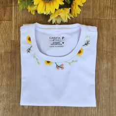 a white t - shirt with sunflowers on the front and back, sitting on a wooden floor