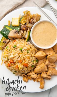 a plate with rice, chicken and vegetables on it next to a cup of sauce