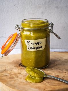 a jar filled with green pest sitting on top of a wooden cutting board next to a spoon