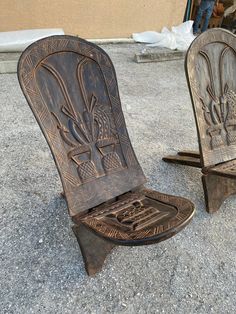 two wooden chairs sitting next to each other on top of a cement ground in front of a building