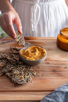 a person dipping some kind of peanut butter into crackers on a cutting board with honey dip in the background