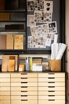 a wooden cabinet with drawers and pictures on the wall next to it is filled with papers