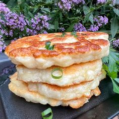 a stack of pancakes sitting on top of a black plate next to purple and green flowers