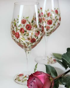 two wine glasses with roses painted on them next to a stemless rose and leaves