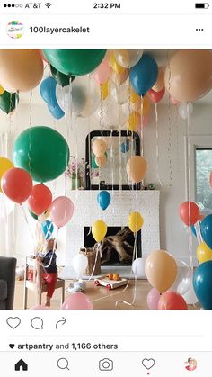 a room filled with lots of balloons and streamers hanging from the ceiling above a fire place