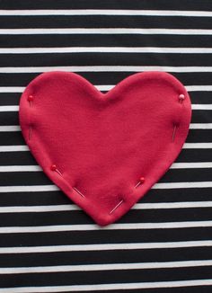 a red heart on top of a black and white striped shirt with pins in the middle