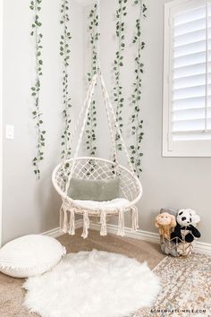 a white hanging chair in the corner of a room with greenery on the wall