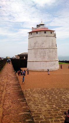 people are walking around in front of a large white tower with a red top on the beach