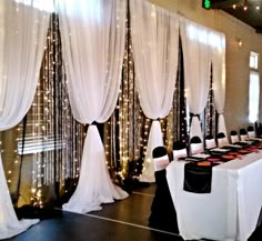 a banquet hall decorated with white drapes and black tablecloths, lights on the wall