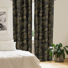 a bed sitting next to a window covered in black and white curtains with gold designs