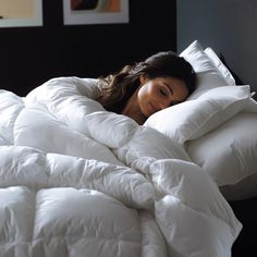 a woman laying in bed with white comforter and pillows