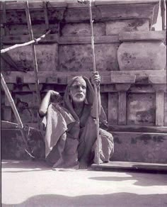 an old black and white photo of a woman sitting on the ground holding onto a pole