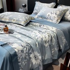 a bed with blue sheets and white flowers on it, next to a night stand