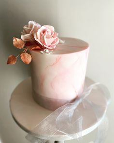 a pink marbled cake with a rose on top and ribbon tied around the edge