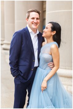 a man and woman standing next to each other in front of a building wearing blue dresses