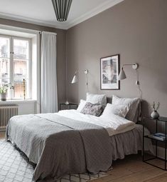 a bedroom with gray walls and white bedding in the corner, along with two windows