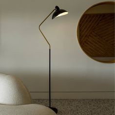 a floor lamp sitting next to a white couch in a room with a round mirror on the wall