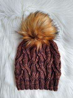 a knitted hat with a fur pom sits on top of a white blanket