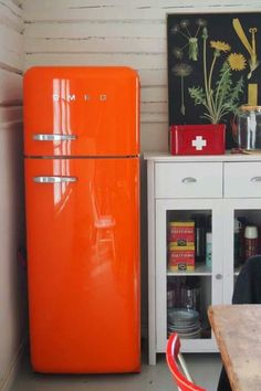 an orange refrigerator in a kitchen next to a wooden table and white cabinet with drawers