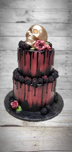 a three tiered cake decorated with blackberries, raspberries and a gold skull