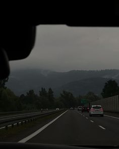 cars driving down the road in front of mountains on a cloudy day with dark clouds