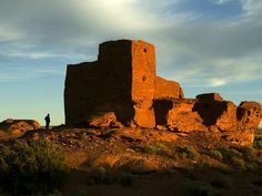 a man standing on top of a rocky hill next to a tall building with a sky background