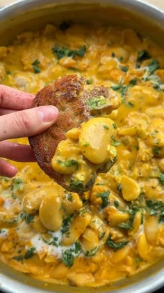 a person holding up a piece of bread over a bowl filled with yellow and green food