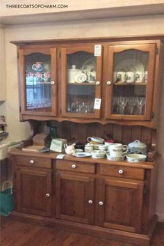 a wooden china cabinet with glass doors and dishes on it's top, next to a dining room table