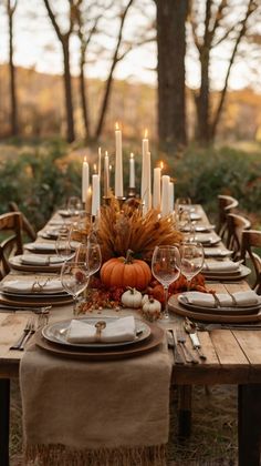 a table set with candles, plates and place settings for an outdoor thanksgiving dinner in the woods