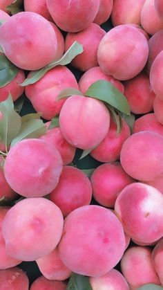 a pile of peaches with leaves on them