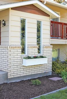 a small brick house with a planter on the front porch and balcony railings