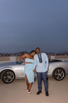 a man and woman standing next to a silver sports car