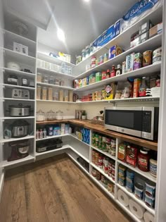 an organized pantry with white shelving and lots of food on the counter top, along with wooden flooring