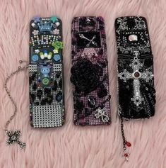 three cell phones are lined up on a pink furnishing with beads and cross charms