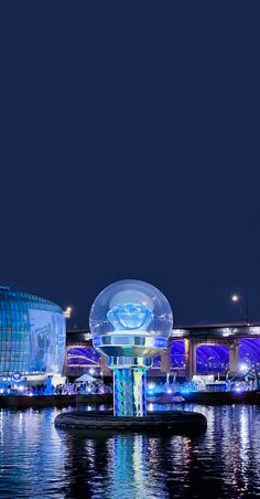 the lights are on and reflecting in the water at night, with an illuminated building in the background