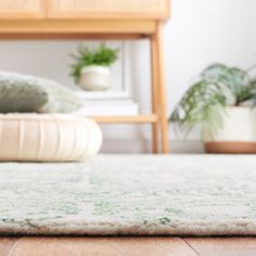 an area rug on the floor in front of a bed with pillows and plants behind it