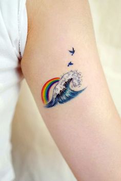 a woman's arm with a rainbow and bird tattoo on it