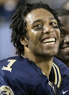 a man with dreadlocks smiles while standing next to another man wearing a football uniform