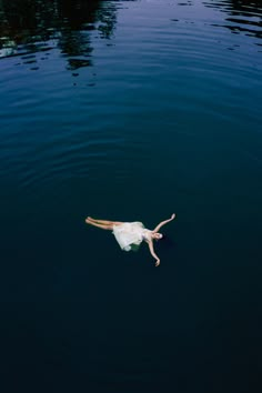 a woman floating on top of a body of water with her arms out in the air