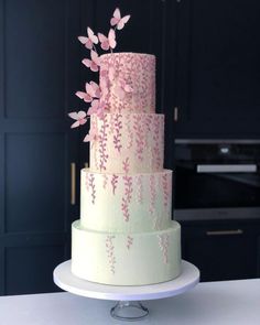 a three tiered cake with pink flowers on it sitting on a table in front of black cabinets